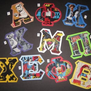 May include: Ten colorful felt letters, each decorated with a different comic book cover. The letters are A, K, M, I, X, E,  Φ, and B.