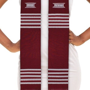 May include: A maroon graduation stole with silver stripes and a key and a building design. The stole is worn by a person with a white sleeveless shirt.