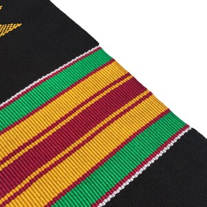 May include: Black woven fabric with a diagonal pattern of green, gold, and burgundy stripes. A white border separates the stripes from the black fabric. A gold star is in the upper left corner.