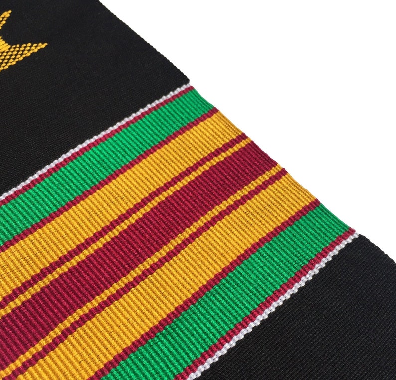 May include: Black woven fabric with a diagonal pattern of green, gold, and burgundy stripes. A white border separates the stripes from the black fabric. A gold star is in the upper left corner.