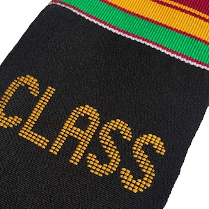 May include: Black graduation stole with gold text reading "CLASS." The stole has a colorful trim of red, green, and gold stripes. The fabric appears to be a textured weave, suitable for a graduation ceremony.