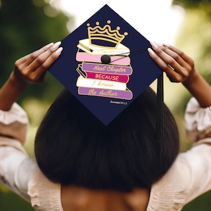 May include: A navy blue graduation cap with a gold crown and stacked books design. The books are pink, purple, and white, with the text "I TRUST THE", "Next Chapter BECAUSE I know the Author" and "Jeremiah 29:11". A black tassel hangs from the cap.
