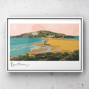 Könnte beinhalten: Ein gerahmter Kunstdruck von Bantham Beach. Die Illustration zeigt eine Küstenlandschaft mit Sandstrand, türkisfarbenem Wasser und einer kleinen Insel mit Gebäuden. Der Himmel ist rosa, und der Druck ist mit "Bantham" signiert.