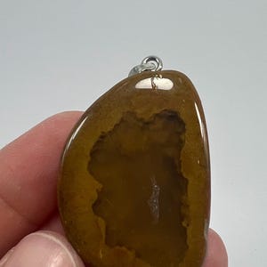 May include: A brown agate pendant with a natural geode opening, featuring a silver bail for attaching a chain.