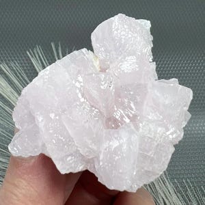 Peut inclure: Un groupe de cristaux translucides rose pâle avec une formation en rosette en couches. Les cristaux ont une apparence délicate, presque givrée.