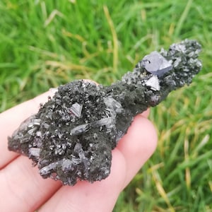 Könnte beinhalten: Ein Cluster aus schwarzen Kristallen mit einem metallischen Glanz auf einer dunkelgrauen Matrix. Die Kristalle sind scharf und haben eine Pyramidenform.