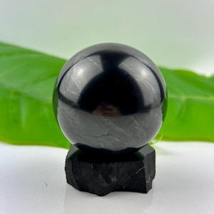 May include: A black obsidian sphere on a black obsidian stand. The sphere is polished and has a reflective surface.
