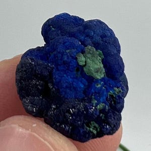 May include: A close-up of an azurite mineral specimen. The stone is a deep blue with areas of green. The surface has a textured, crystalline appearance. The mineral's colours create a striking contrast, highlighting its natural beauty.