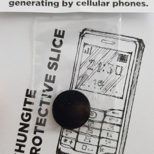 Puede incluir: Una rodaja protectora de shungita negra, un pequeño disco redondo, se muestra sobre un fondo blanco con un dibujo en blanco y negro de un teléfono móvil. El texto "Shungite Protective Slice" está impreso en el lado izquierdo de la imagen. El texto "21:30" es visible en la pantalla del teléfono.