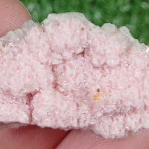 Puede incluir: Un cúmulo de pequeños cristales delicados de color rosa y blanco. Los cristales están agrupados en una formación natural rugosa.