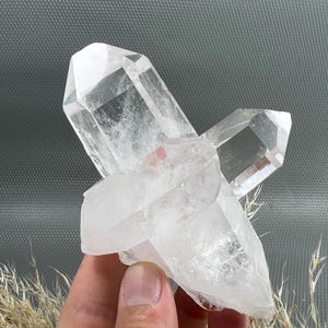 Op de afbeelding: Een helder kwartskristalcluster met meerdere puntige uiteinden en doorschijnende facetten. Het mineraalexemplaar vertoont natuurlijke interne insluitingen en scherpe geometrische randen, wat een complex groeipatroon laat zien.