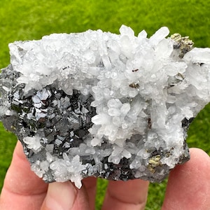 May include: A cluster of clear quartz crystals with black and silver metallic minerals. The quartz crystals are clustered together in a dense formation, with some of the crystals being longer than others. The metallic minerals are scattered throughout the cluster, adding a touch of sparkle and contrast.