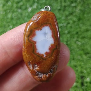 May include: A brown agate pendant with a white center and a silver bail. The agate has a natural, rough texture.