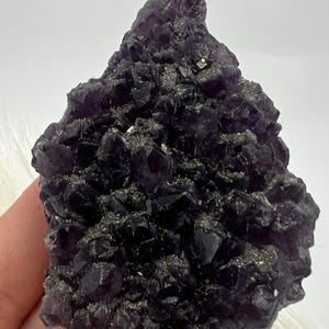 以下が含まれることがあります： 濃いグレーでほぼ黒に近い、紫色の蛍石の結晶の塊。結晶は、荒々しい自然な形で集まっています。