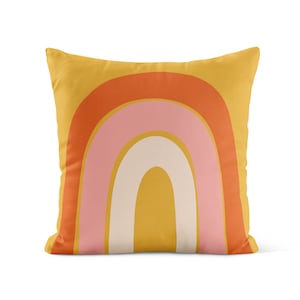 Puede incluir: Una almohada amarilla con un dise&ntilde;o de arco&iacute;ris en tonos naranja, rosa y blanco.