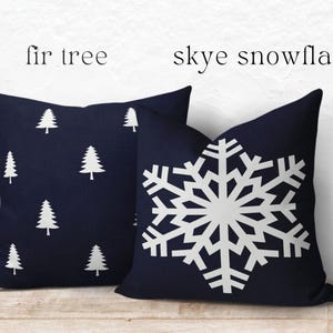 May include: Two square throw pillows in dark navy blue. The left pillow features a repeating white fir tree pattern, labeled 'fir tree'. The right pillow displays a large, centered white snowflake design, labeled 'skye snowflake'.