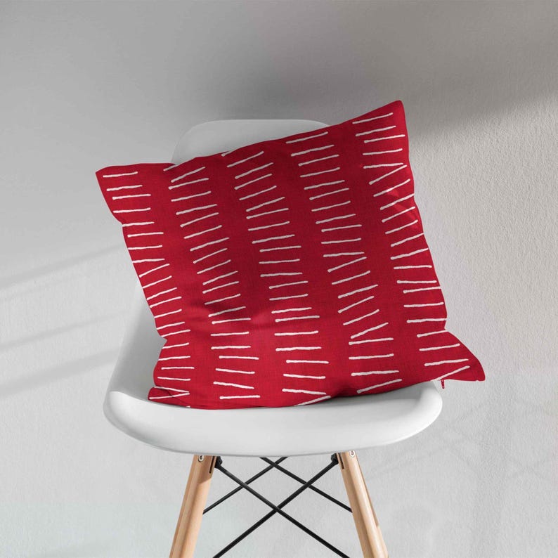 Peut inclure: Un coussin carr&eacute; dot&eacute; d'une base en tissu rouge profond avec un motif r&eacute;p&eacute;titif de courtes lignes blanches horizontales en pointill&eacute;s, dispos&eacute;es en colonnes verticales sur toute la surface pour cr&eacute;er un effet visuel textur&eacute;.