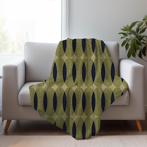 May include: A throw blanket with a repeating pattern of olive green ovals and navy blue elongated ovals. The blanket is draped over a white sofa. The design has a retro, mid-century modern aesthetic.