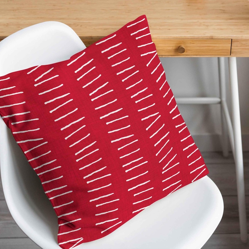 Peut inclure: Un coussin carr&eacute; pr&eacute;sentant une couleur de base rouge vif avec un motif r&eacute;p&eacute;titif de courtes lignes blanches horizontales en pointill&eacute;s, dispos&eacute;es en colonnes verticales sur toute la surface de la housse en tissu.