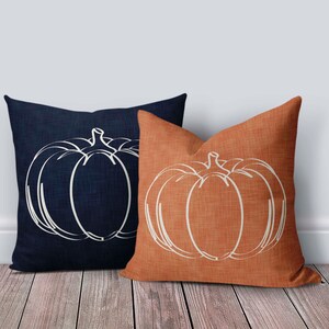 May include: Two decorative throw pillows with a white outline of a pumpkin on a dark blue and orange background.