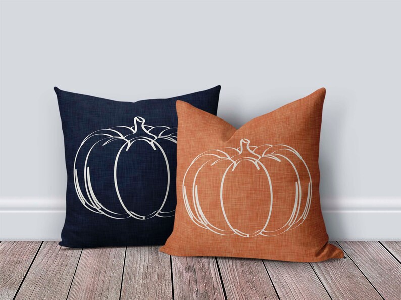 May include: Two decorative throw pillows with a white outline of a pumpkin on a dark blue and orange background.