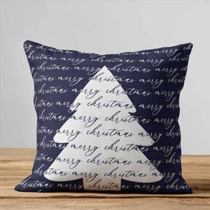 May include: A square throw pillow featuring a dark navy blue background with a repeating white cursive script pattern that reads merry christmas. A large, solid white silhouette of a Christmas tree is centered on the front of the pillow.