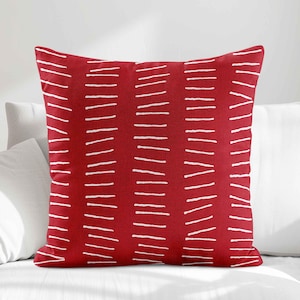 Peut inclure: Un coussin carr&eacute; dot&eacute; d'une base en tissu rouge vif, orn&eacute; d'un motif r&eacute;p&eacute;titif de colonnes verticales compos&eacute;es de courtes lignes blanches horizontales dessin&eacute;es &agrave; la main, cr&eacute;ant un effet visuel textur&eacute; sur toute la surface.