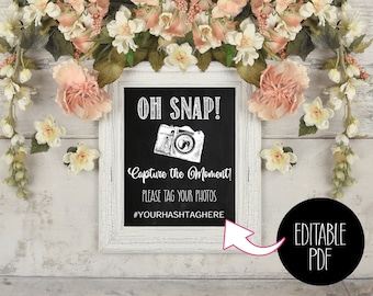 May include: White framed chalkboard sign with the text "OH SNAP! Capture the Moment! Please tag your photos #YOURHASHTAGHERE" and a black and white illustration of a camera. The sign has a pink arrow pointing to the text "EDITABLE PDF" in a black circle.