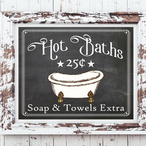 May include: A vintage-style sign with a chalkboard background and white lettering. The sign reads "Hot Baths 25¢ Soap & Towels Extra". A drawing of a white bathtub with gold feet is in the center of the sign.