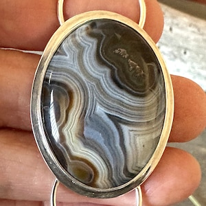 May include: A silver oval pendant with a brown and white agate stone. The stone has a swirling pattern of white, brown, and gray.