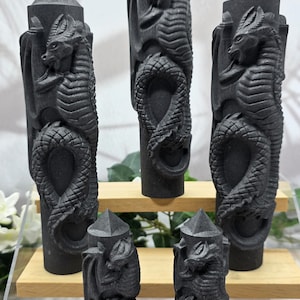 May include: Five dark gray dragon-themed decorative pillars. Each pillar features a detailed dragon carving with a serpent-like body and a pointed top. The pillars are displayed on wooden shelves.