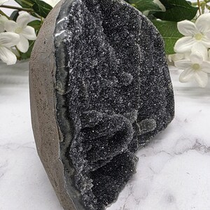 May include: A dark gray geode with a sparkling, crystal-like interior. The geode has a rough, textured exterior and a smooth, polished interior. The geode is a natural stone formation, and it is a unique decorative item.