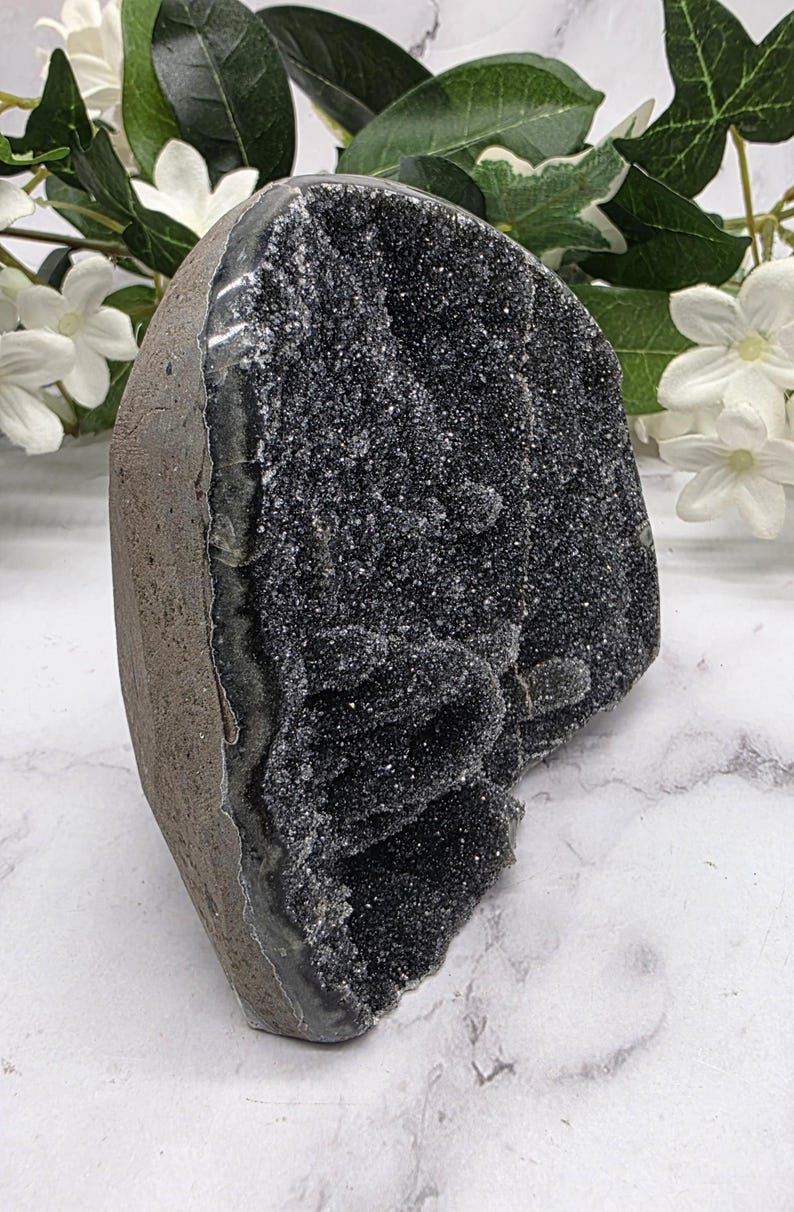May include: A dark gray geode with a sparkling, crystal-like interior. The geode has a rough, textured exterior and a smooth, polished interior. The geode is a natural stone formation, and it is a unique decorative item.