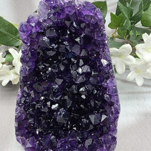 May include: A large, raw amethyst geode with a deep purple hue. The crystal formation is dense and sparkling, with a mix of dark and light shades. The geode is a natural, uncut specimen, showcasing the beauty of the mineral.