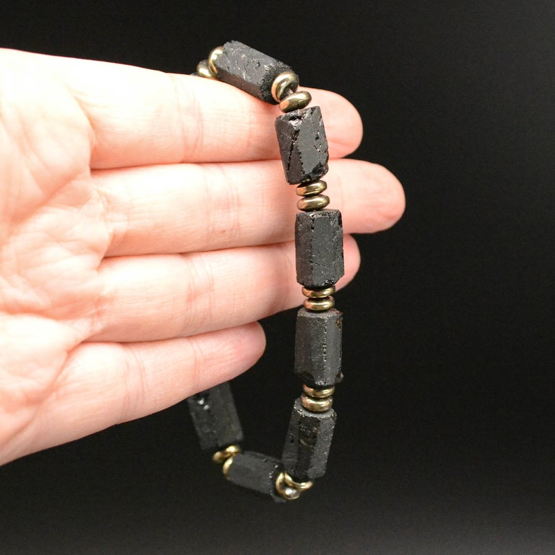 May include: Black beaded bracelet with gold spacers. The beads are rectangular and have a rough, textured surface.