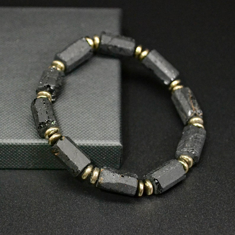 May include: A black lava rock bracelet with gold accents. The bracelet is made of round beads with a rough, textured surface.