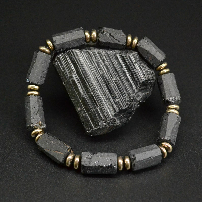 May include: Black Tourmaline bracelet with gold accents. The bracelet is made of black tourmaline beads and gold spacers. The bracelet is shown on a black background with a large black tourmaline crystal.
