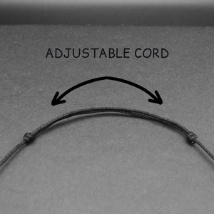 May include: A black adjustable cord necklace with a sliding knot. The text "ADJUSTABLE CORD" is written above the cord.