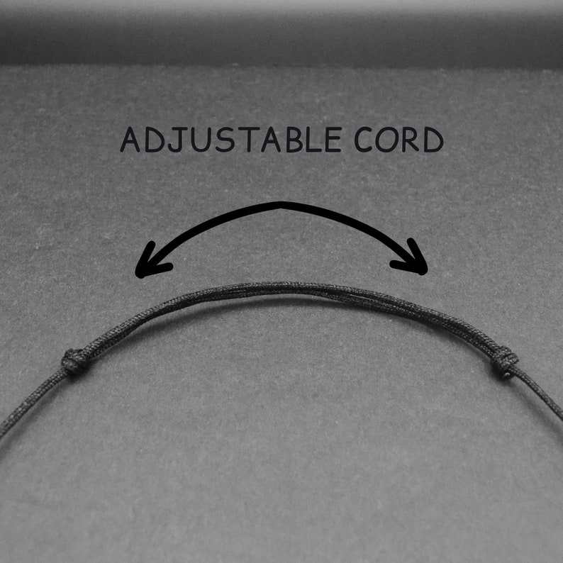 May include: A black adjustable cord necklace with a sliding knot. The text "ADJUSTABLE CORD" is written above the cord.