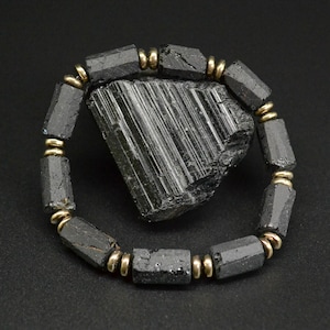 May include: Black Tourmaline bracelet with gold accents. The bracelet is made of black tourmaline beads and gold spacers. The bracelet is shown on a black background with a large black tourmaline crystal.