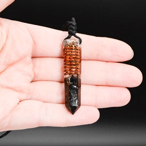 May include: A black and copper crystal pendant with a copper wire wrapped around the center. The pendant is hanging from a black cord.