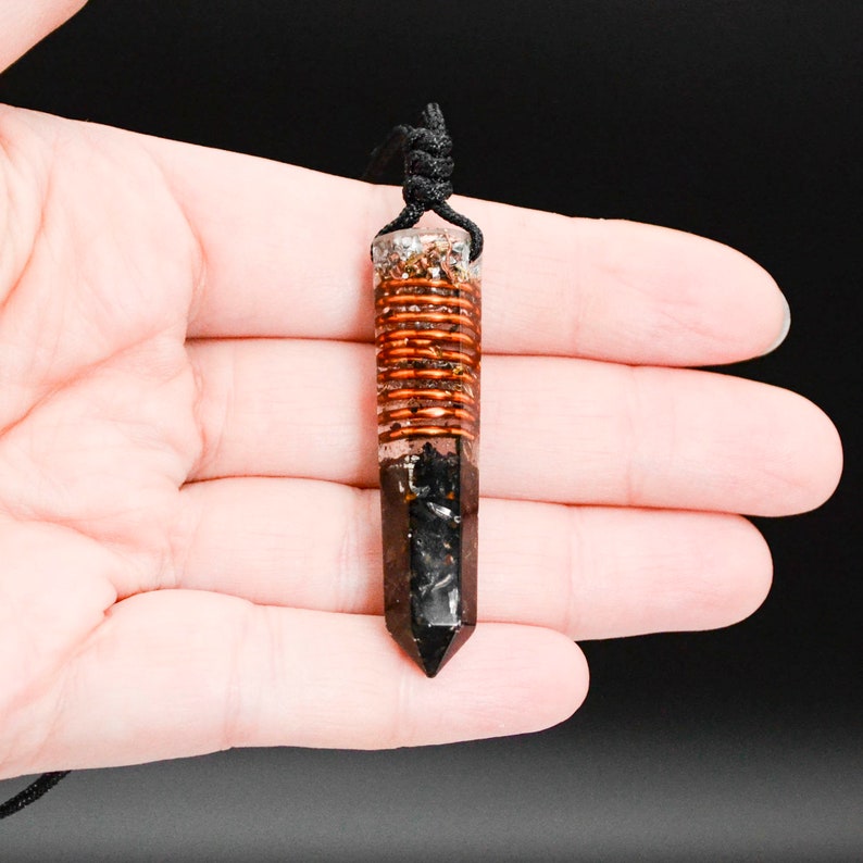 May include: A black and copper crystal pendant with a copper wire wrapped around the center. The pendant is hanging from a black cord.
