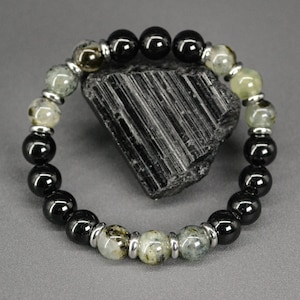Può includere: Braccialetto di pietre preziose nere e verdi con perline d'argento. Il braccialetto è appoggiato su una pietra nera.