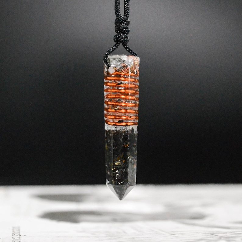 May include: A clear quartz crystal pendant with a copper wire wrapped around the center. The pendant is attached to a black cord.