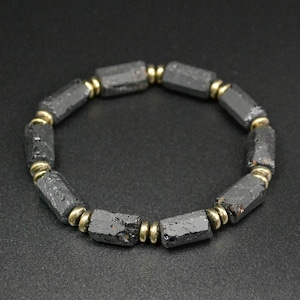 May include: A black beaded bracelet with gold accents. The beads are made of black lava rock and are shaped like small cylinders. The bracelet is made of natural materials and has a rustic look.