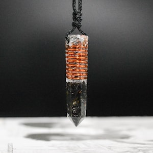May include: A black and clear crystal pendant with a copper wire wrapped around the center. The pendant is attached to a black cord.
