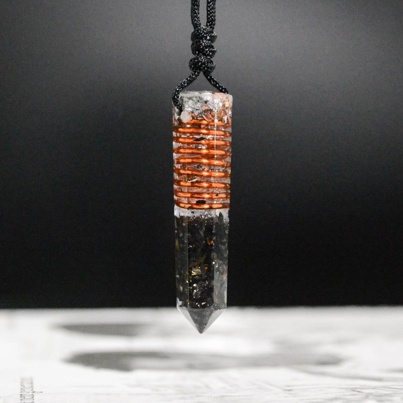 May include: A black and clear crystal pendant with a copper wire wrapped around the center. The pendant is attached to a black cord.