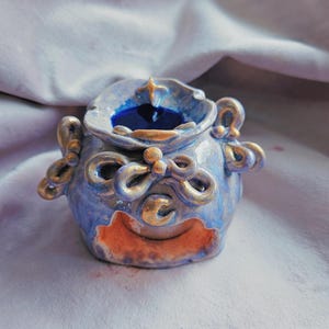 Könnte beinhalten: Ein blauer und goldener Keramik-Räucherofen mit einem dekorativen Design aus Schleifen und einem Halbmond. Der Ofen hat ein kleines Loch im Boden für ein Teelicht.