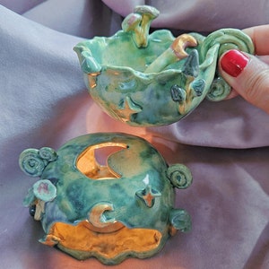 May include: A green ceramic incense burner with a moon and stars design. The burner is in two pieces, with the top piece featuring a mushroom and a crescent moon.