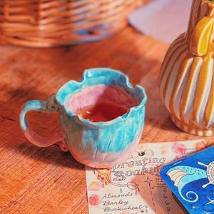 May include: A yellow and white striped ceramic vase containing pink flowers, a blue and pink ruffled ceramic mug, a deck of blue tarot cards with a central star design, and a paper chart titled Sprouting Soaking with handwritten text.